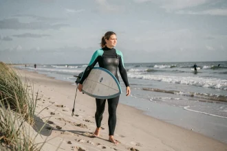 Débutante en surf tenant un longboard sur la plage d'Anglet à marée basse avec des vagues douces en arrière-plan