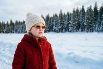 Jeune fille portant des lunettes de soleil et un manteau rouge en hiver dans un champ enneigé