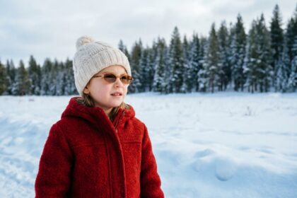 Jeune fille portant des lunettes de soleil et un manteau rouge en hiver dans un champ enneigé